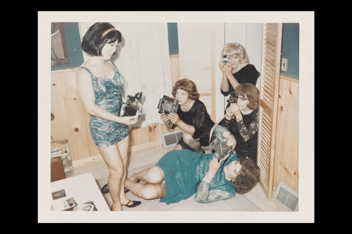  A group of women all wearing dresses, some black some green, and they all squat and stand as they take photos of one another.